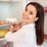 Uśmiechnięta kobieta wyjmuje jajka z lodówki